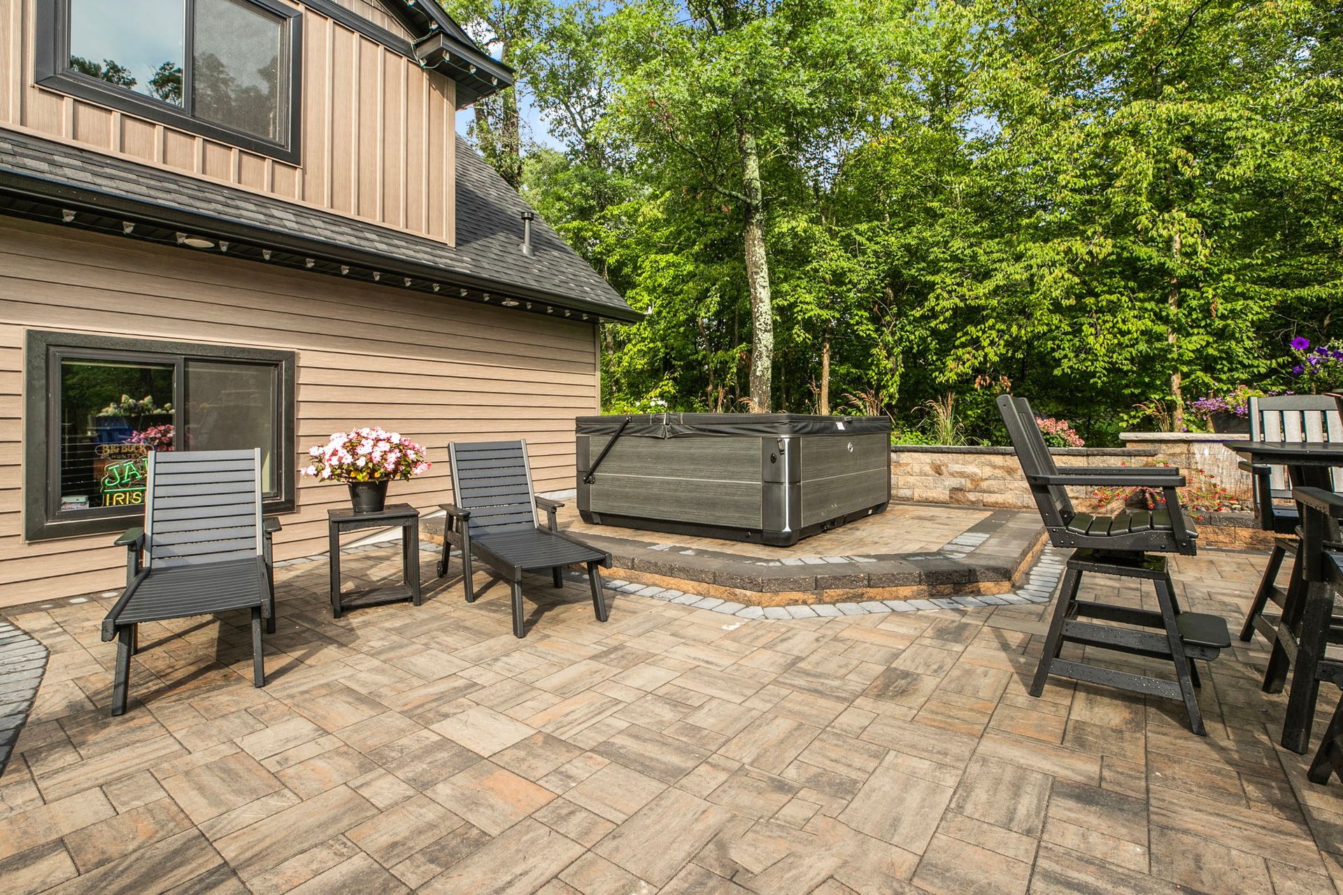 Patio with outdoor chairs, table, and raised planter beside a house, backed by trees