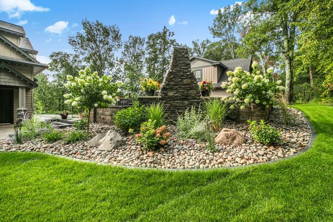 Landscaped garden bed with a stone fountain, shrubs, flowers, and lush green lawn beside a house