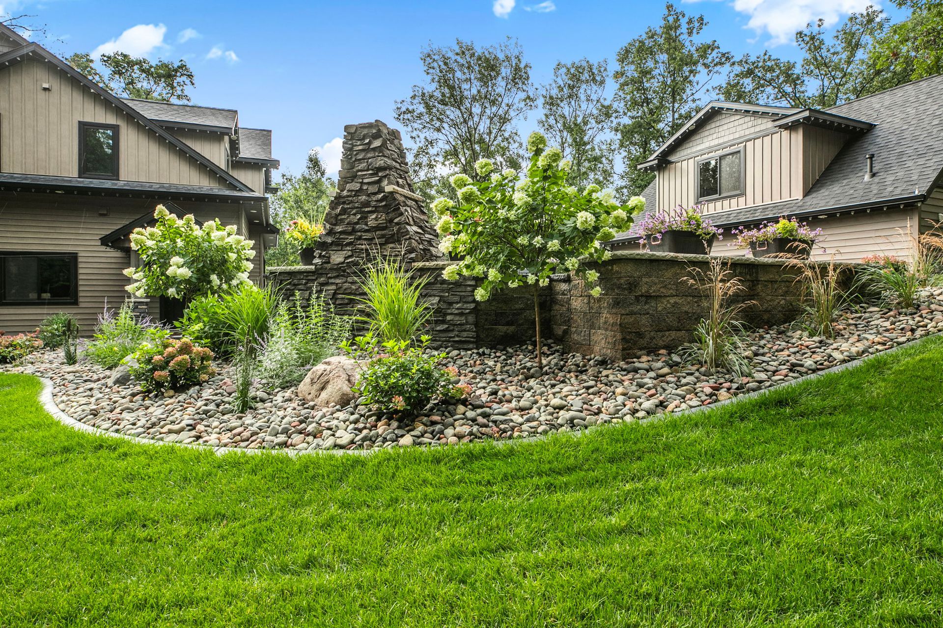 Landscaped rock garden with a stone fountain, green lawn, and houses in the background