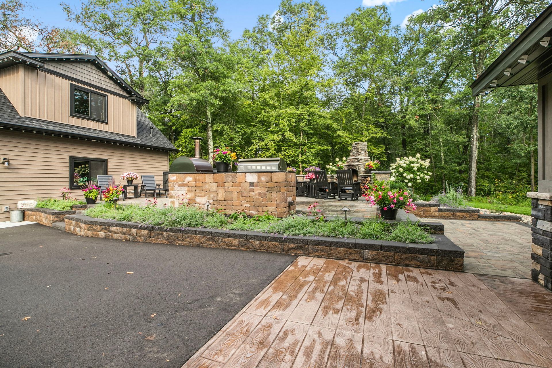 Backyard patio with stone retaining wall, potted plants, and trees beside a house