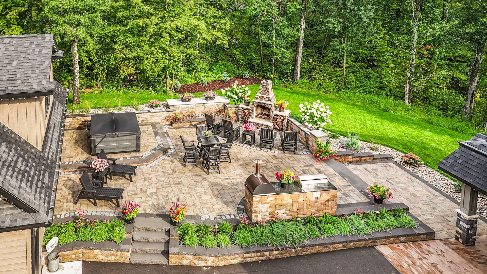 Stone patio with outdoor dining tables, potted plants, and a lush green garden backdrop