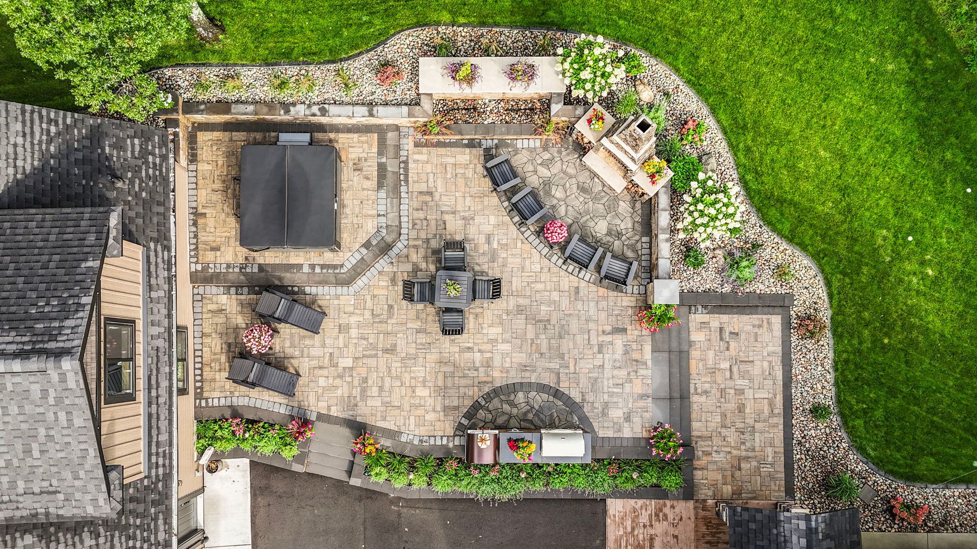 Aerial view of a stone patio with outdoor seating, planters, and a small grill beside a green lawn