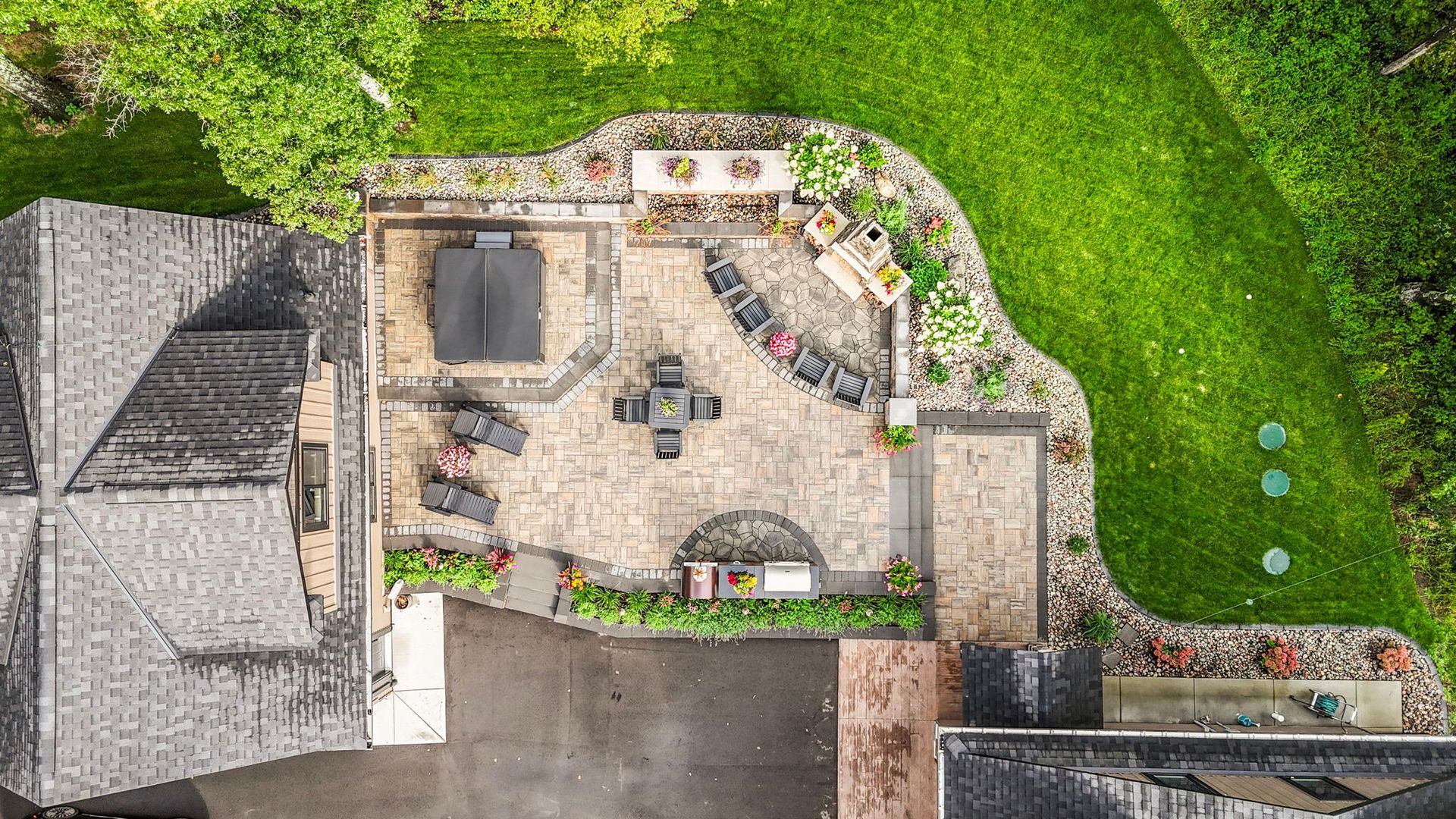 Aerial view of a backyard patio with outdoor seating, a grill, and surrounding green lawn.