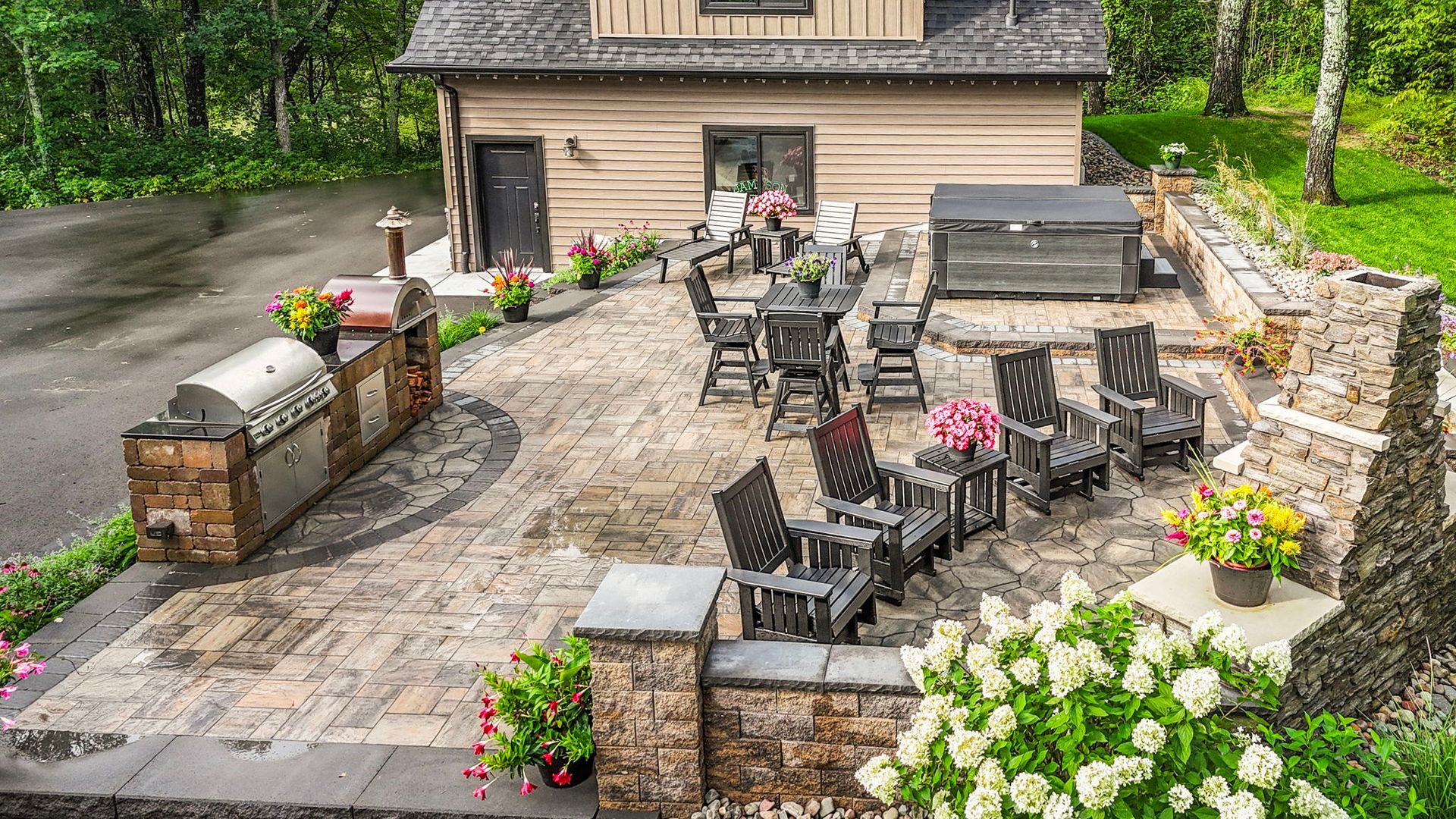 Stone patio with outdoor dining and lounge furniture, flower planters, and a built-in grill beside a house
