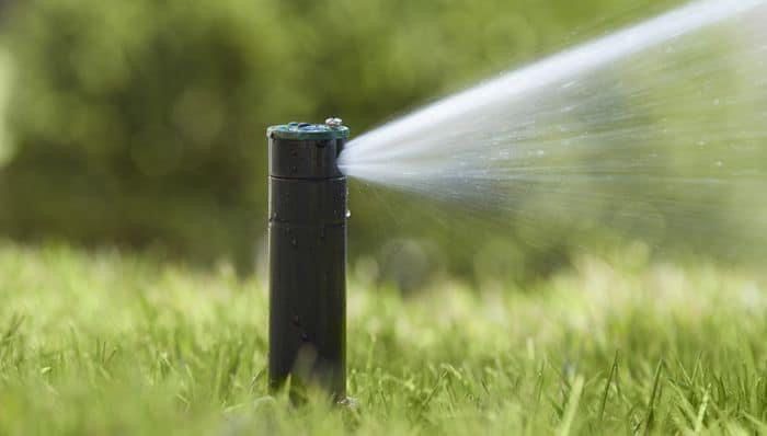 Black lawn sprinkler spraying water over green grass outdoors