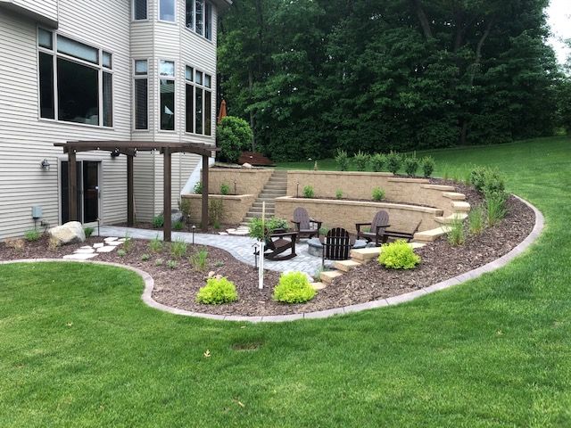 Backyard patio with stone retaining wall, seating, and landscaped garden beside a house
