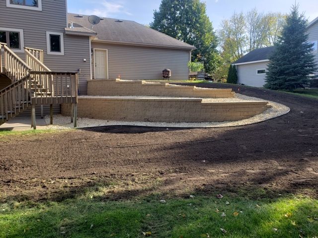 Backyard with new stone retaining wall and curved concrete patio beside a tan house