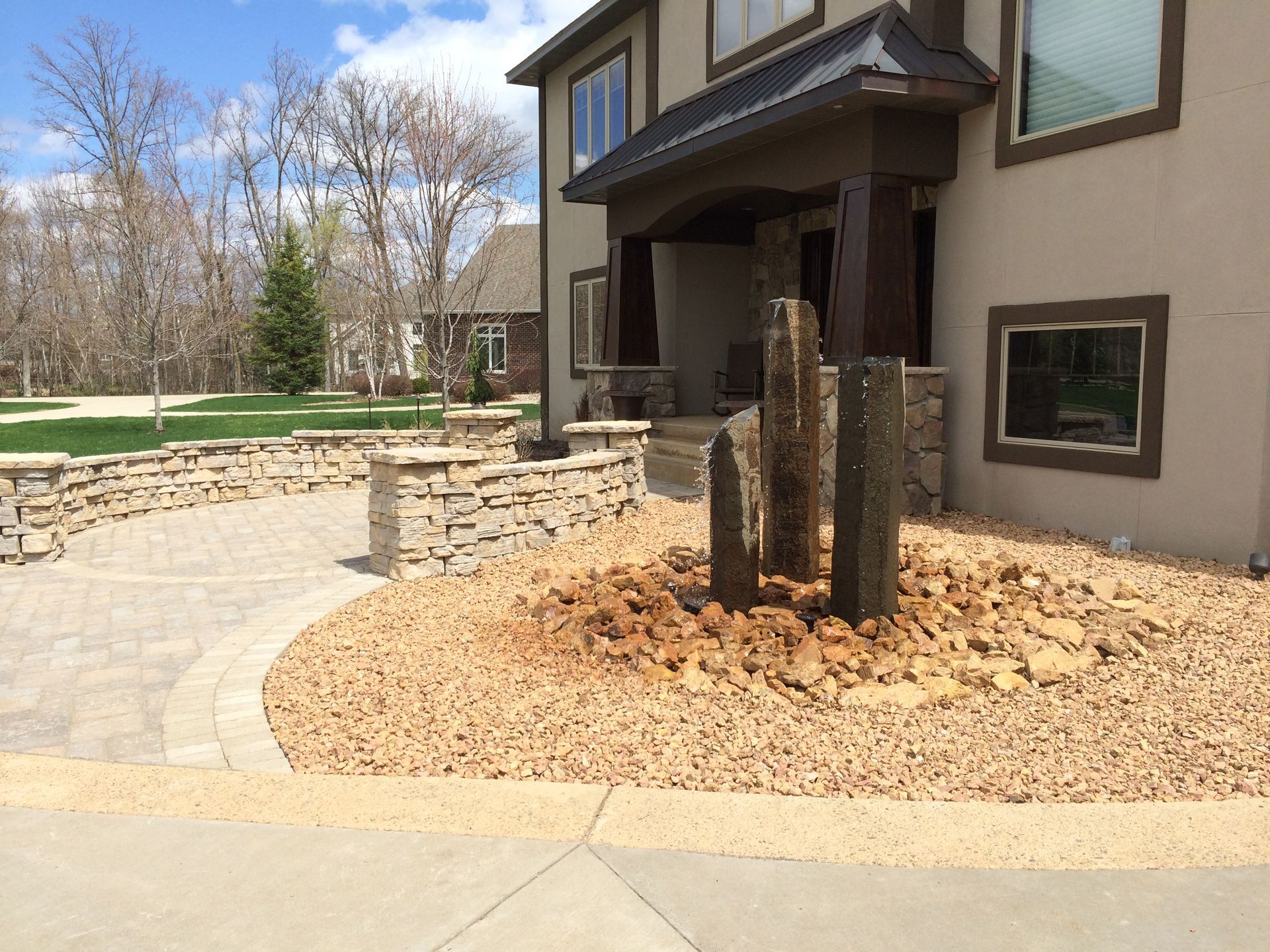 Modern house exterior with stone walkway, landscaped rock bed, and three wooden posts in front