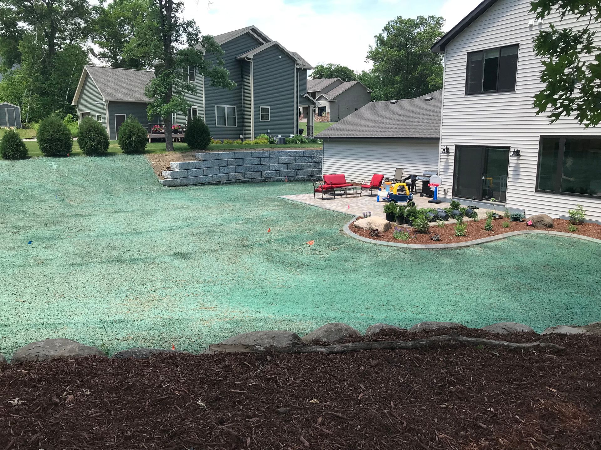 Suburban backyard with fresh green lawn, stone retaining wall, and houses in the background