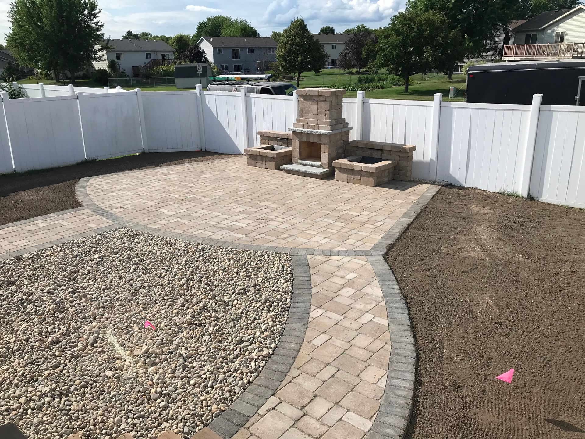 Backyard with gravel paths, stone patio, white fence, and a brick outdoor fireplace.