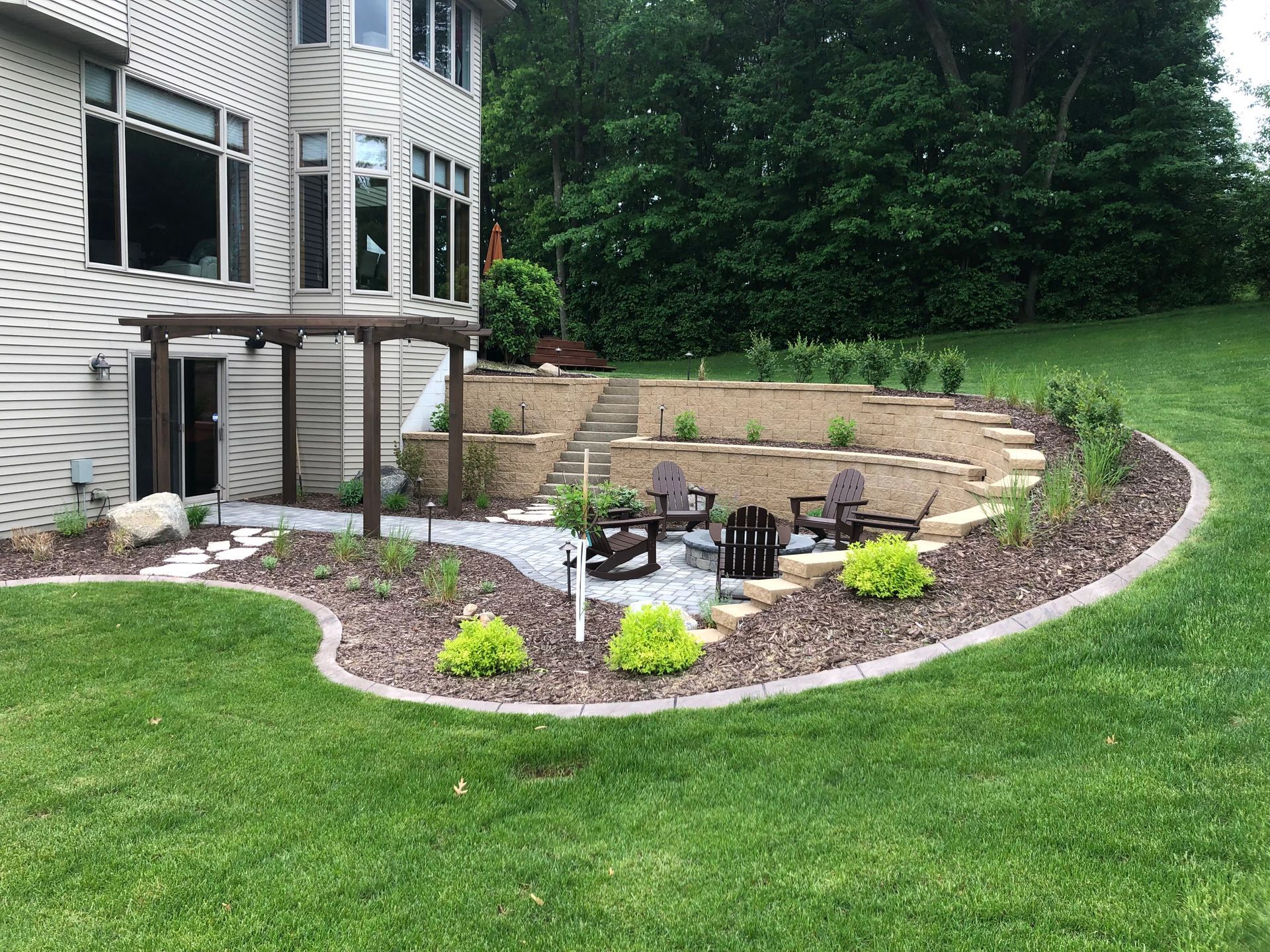 Backyard patio with stone seating wall, fire pit, and landscaped garden beside a house