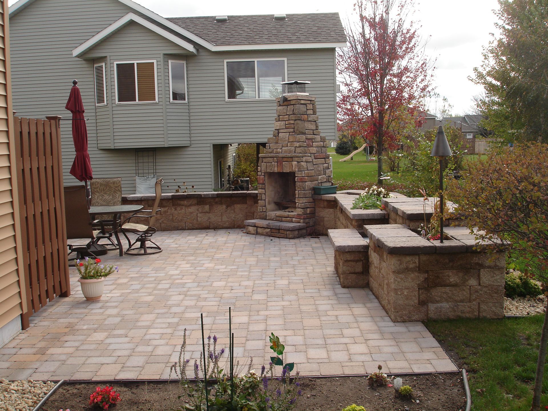 Back patio with stone pavers, built-in seating, stone fireplace, and a house in the background