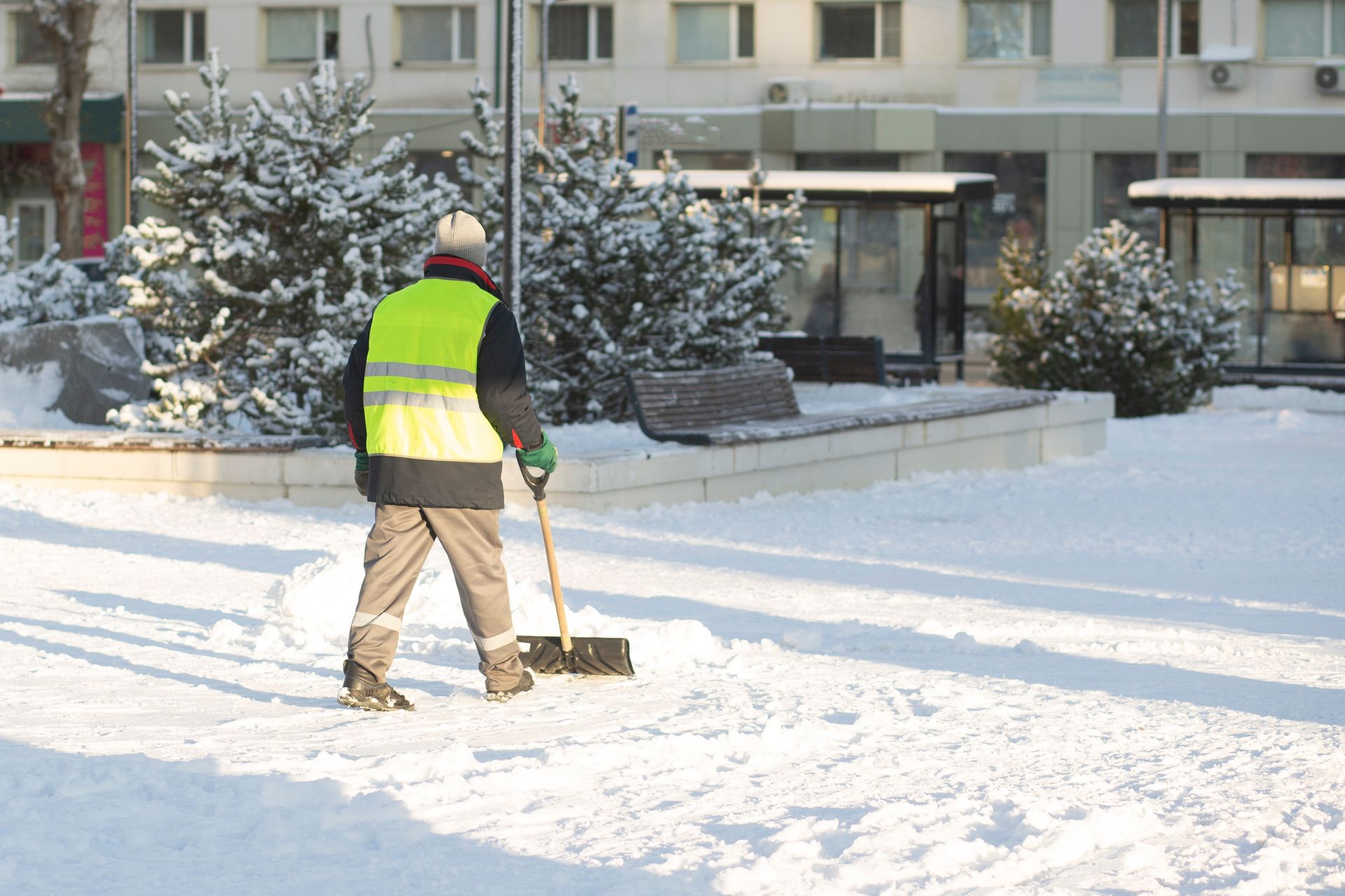 Person in a neon safety vest shoveling snow on a residential sidewalk in front of an apartment building