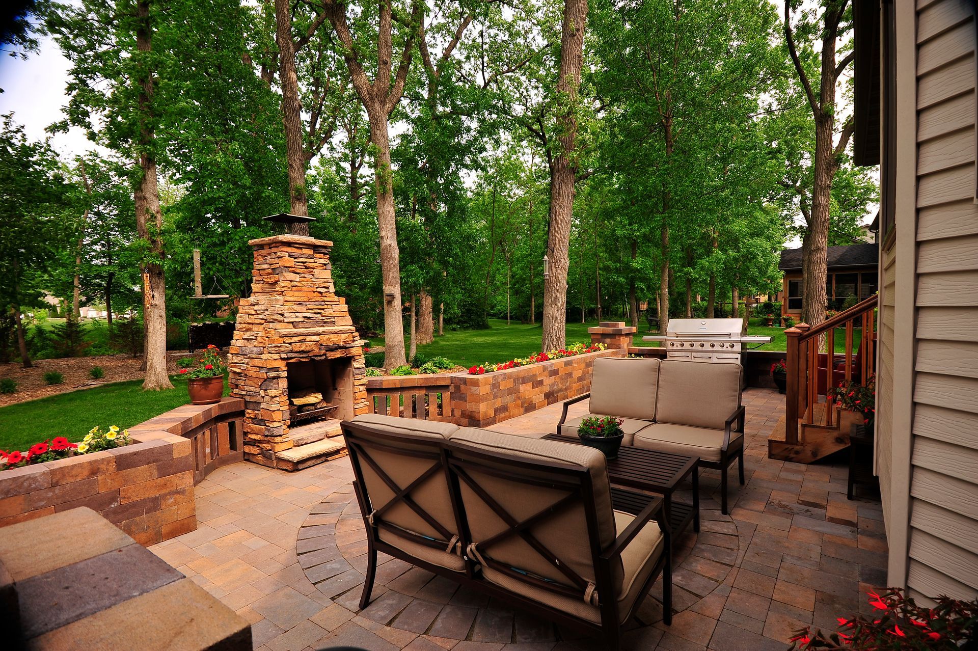 Backyard patio with brick fireplace, cushioned seating, and trees in a wooded setting