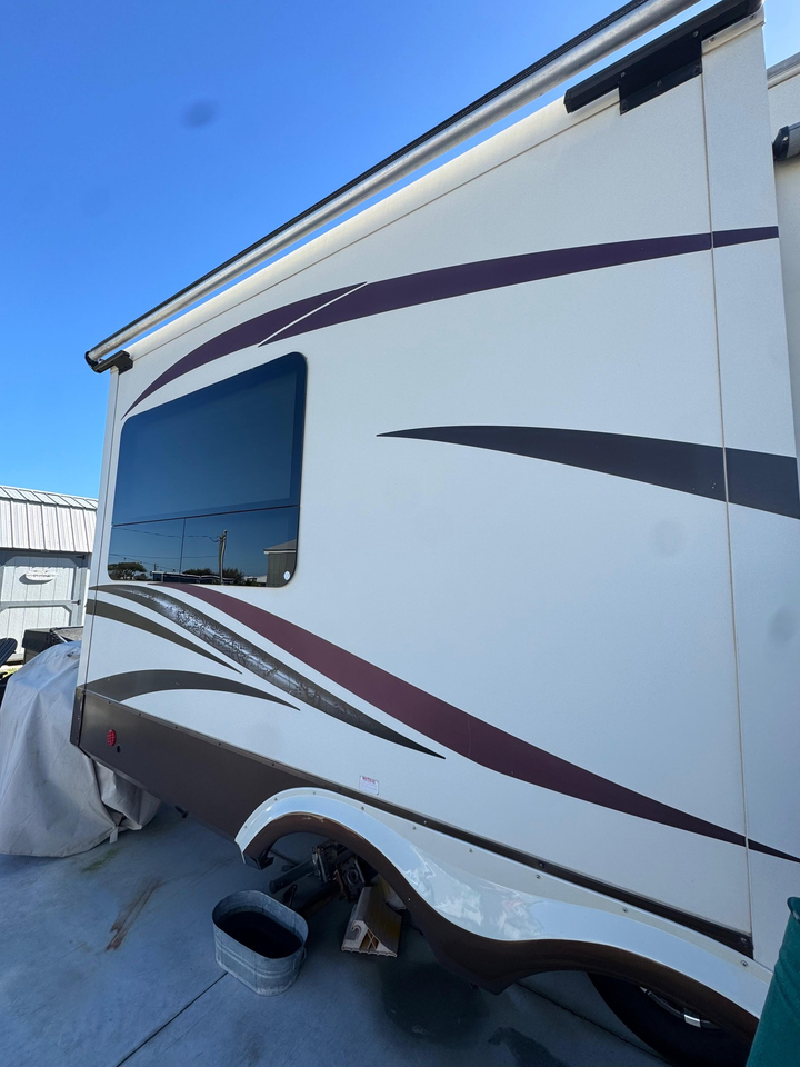 Side view of a white and brown recreational vehicle parked outdoors under a bright blue sky.