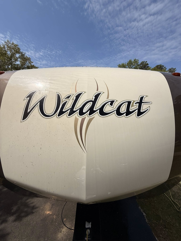 The front cap of a beige Wildcat RV under a bright blue sky, featuring the brand name in black stylized lettering.