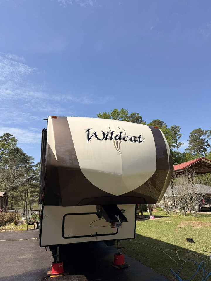 A tan and brown Wildcat fifth-wheel camper parked on an asphalt driveway under a clear blue sky.