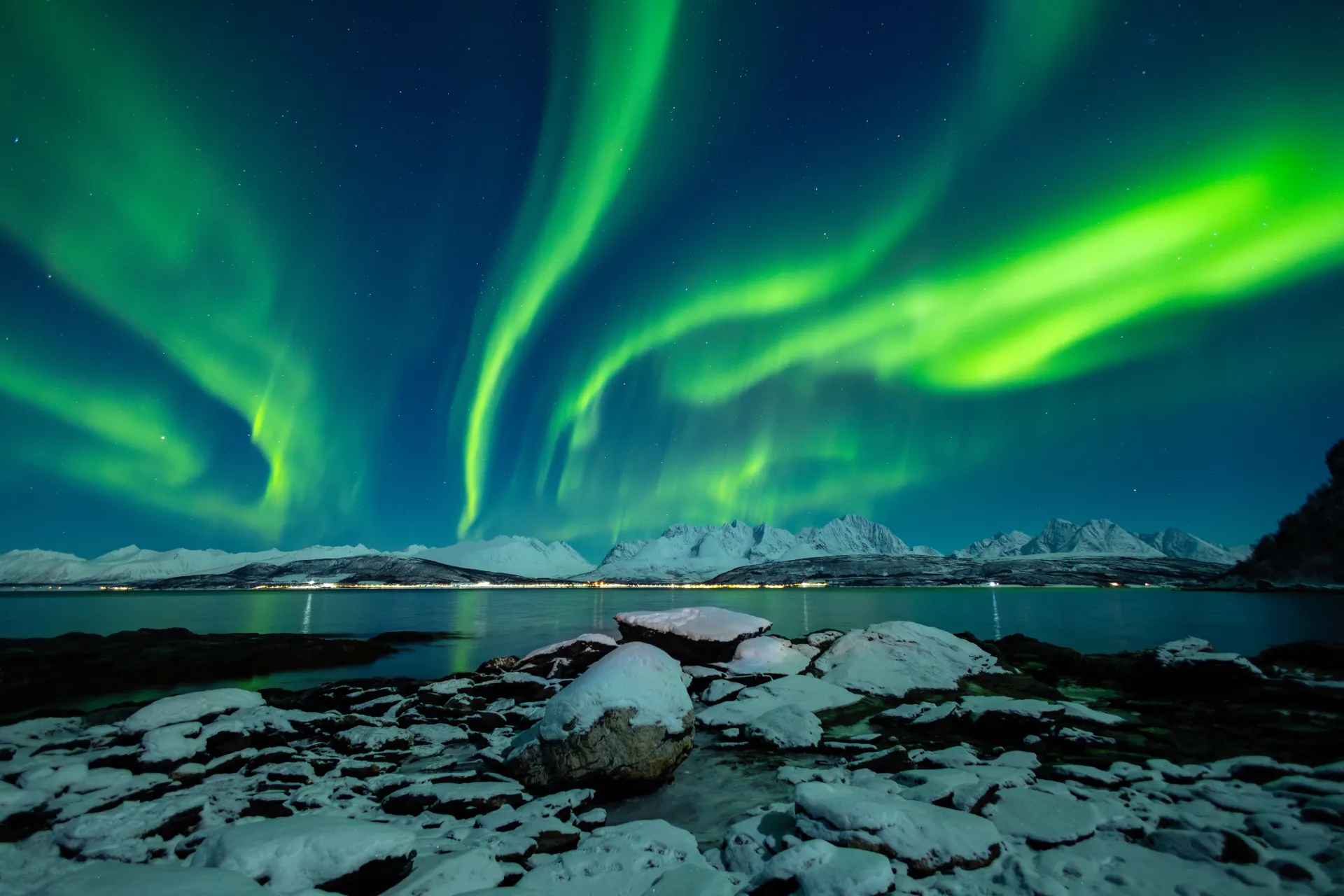 Green northern lights over snowy mountains near Tromsø