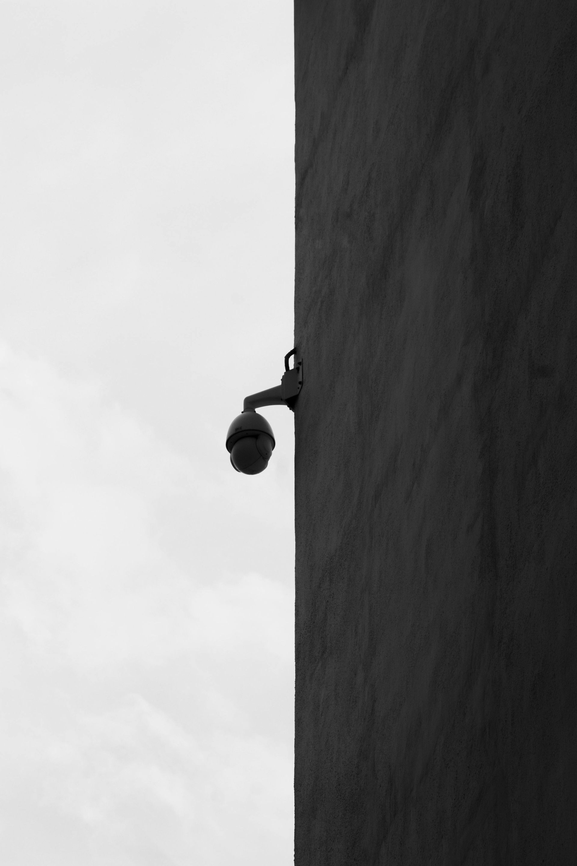 A black and white photo of a security camera on the side of a building.