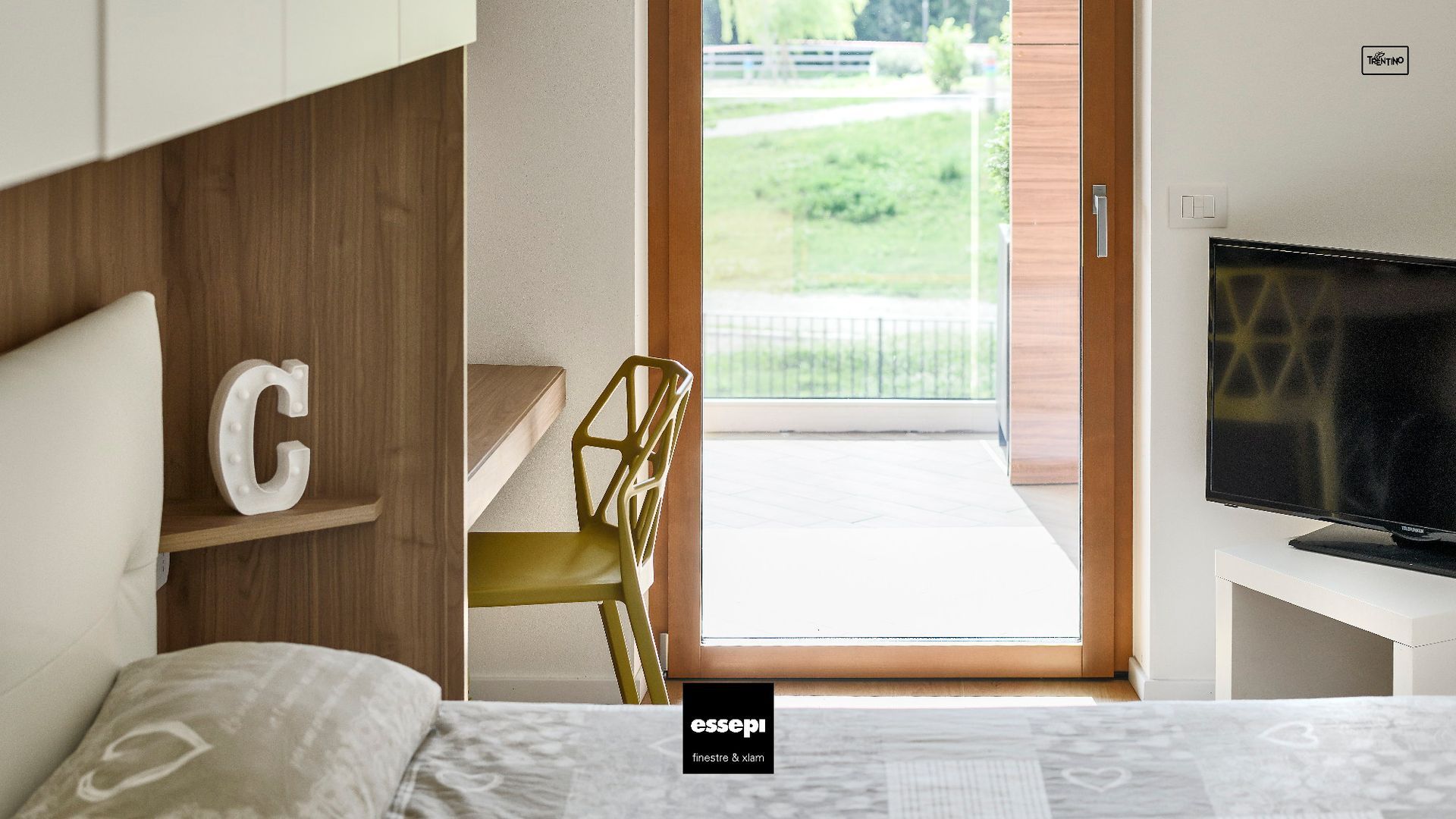 Camera da letto con scrivania in legno, sedia gialla e porta a vetri che dà sul patio;
