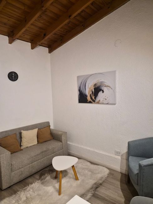 Acogedora sala de estar con sofá beige, sillón azul, mesa de centro blanca, alfombra y arte abstracto en las paredes blancas.