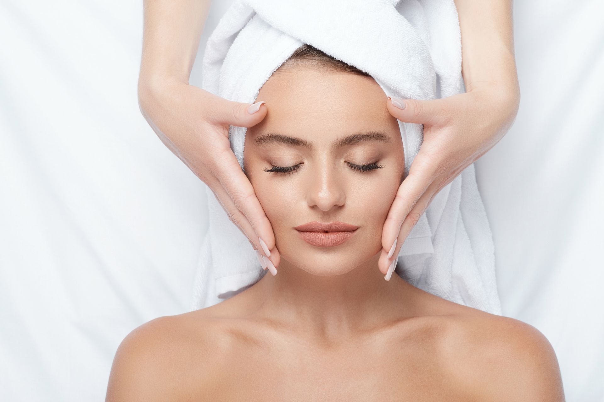 A woman with a towel wrapped around her head is getting a facial massage.