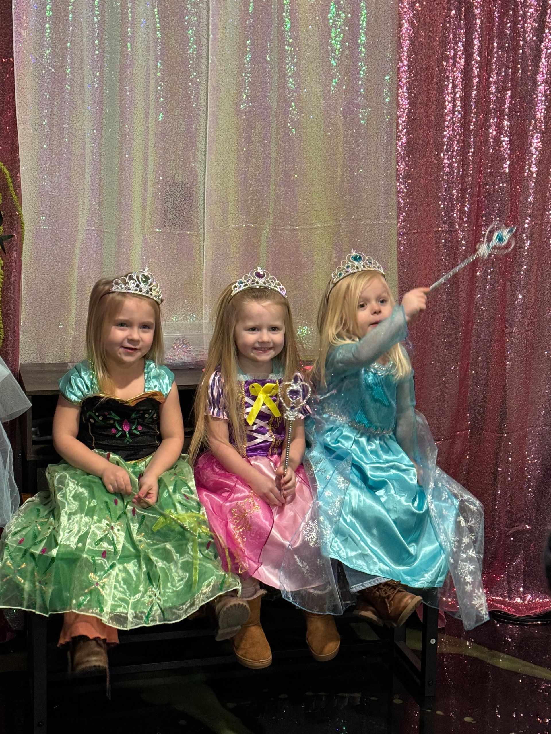 Three little girls dressed as princesses are sitting next to each other on a chair.