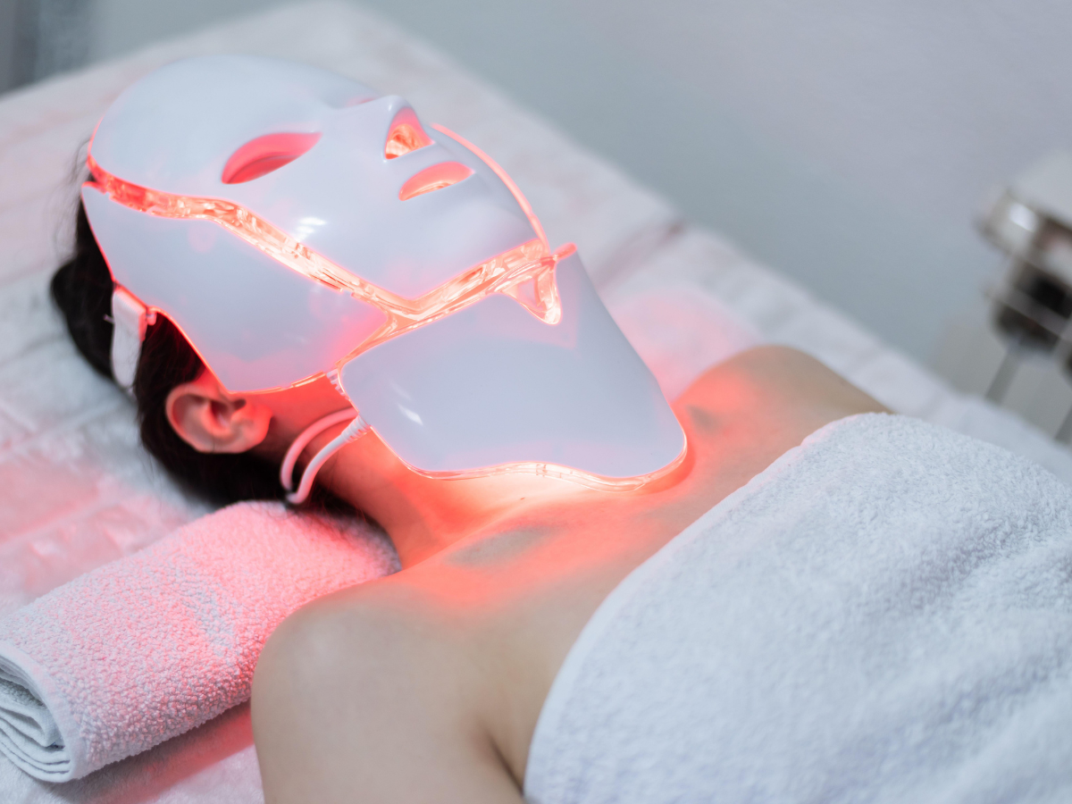 A woman is laying on a bed with a led mask on her face.