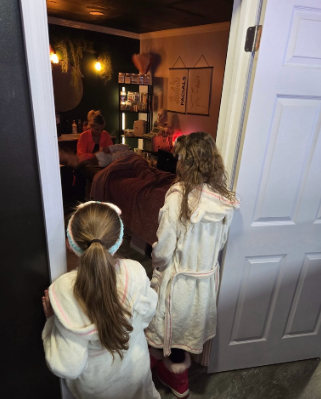 Two girls in bathrobes are standing in a doorway looking into a room.