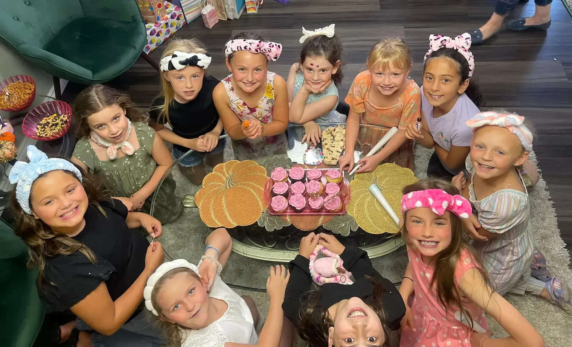 A group of young girls are sitting around a table with a cake.