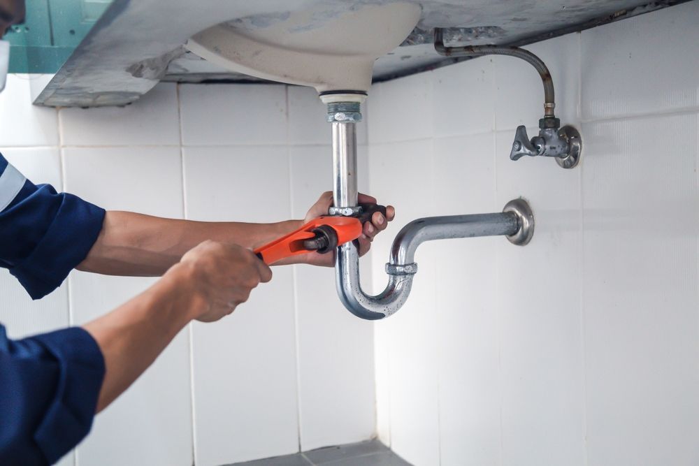 A plumber is fixing a sink pipe with a wrench.