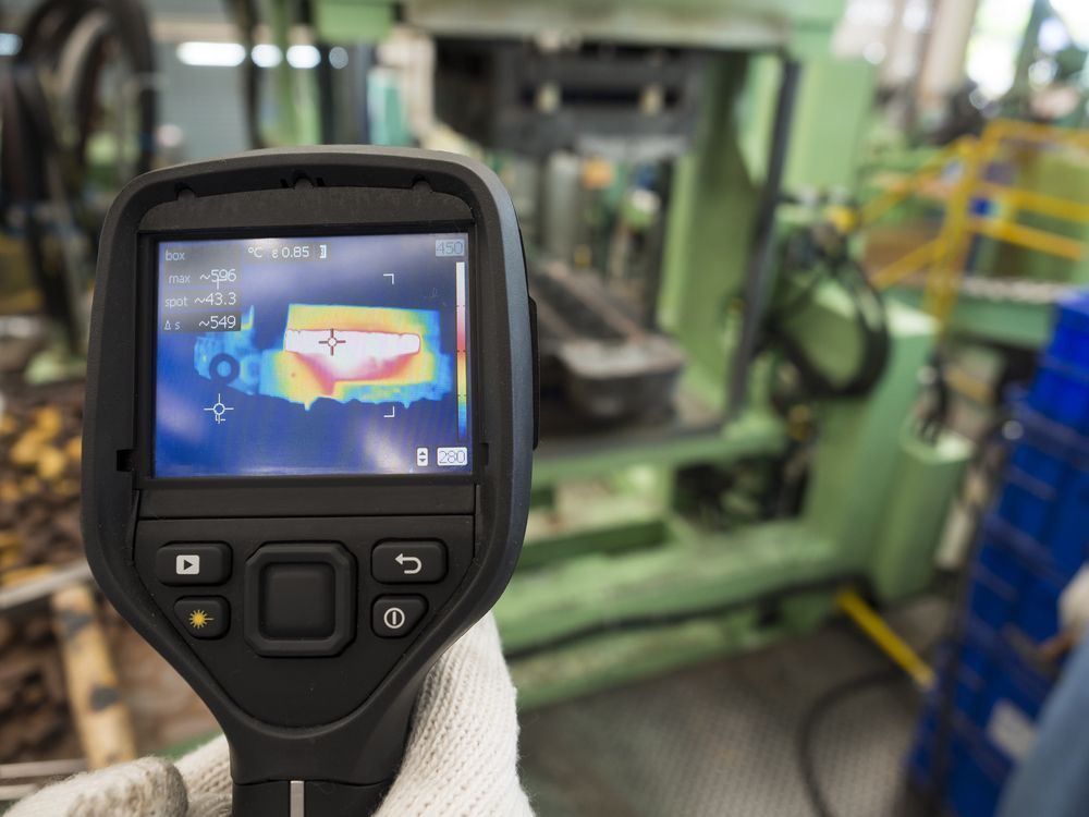A person is holding a thermal camera in a factory.