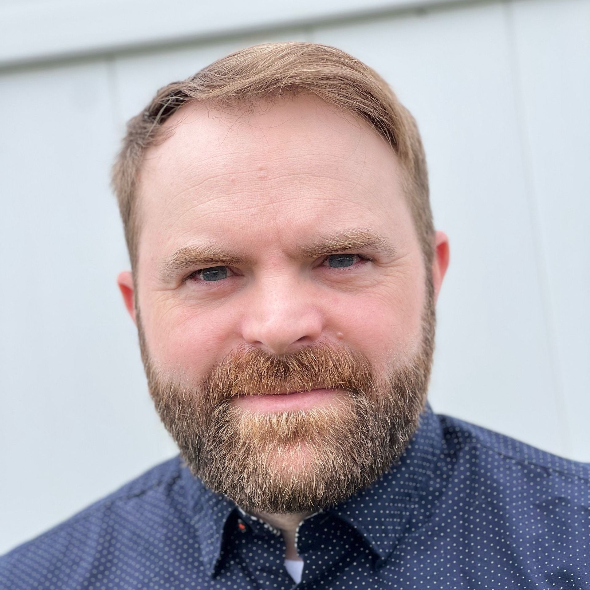 Man with a full beard, wearing a dark blue button-down shirt, looking directly at the camera.