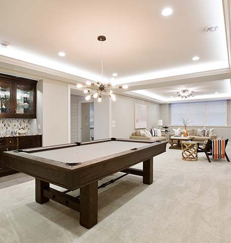 A basement game room featuring a wood pool table, recessed lighting, and a lounge area with seating and a wet bar.