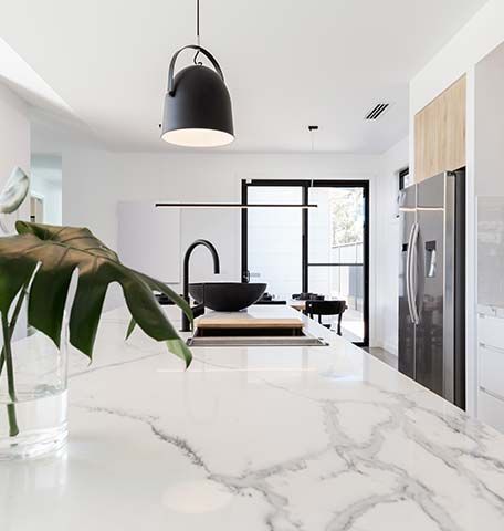 A modern kitchen with a white marble island, a black sink, and an aesthetic theme
