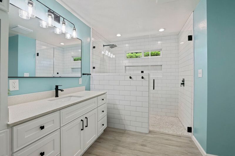 A modern bathroom with a white vanity, a large mirror, and a walk-in shower featuring white subway tiles and light blue walls.