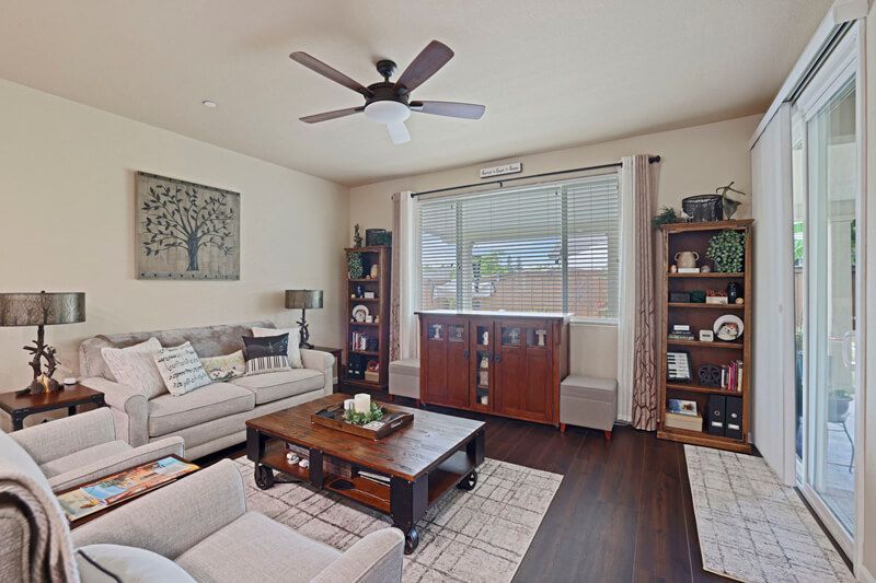 A cozy living room with a sofa, two chairs, a wood coffee table, a ceiling fan, and wooden bookshelves on dark floors.