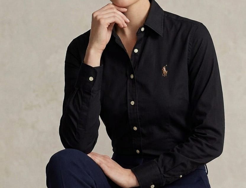 Una persona con una camisa negra abotonada está sentada contra una pared beige, apoyando la barbilla en la mano.