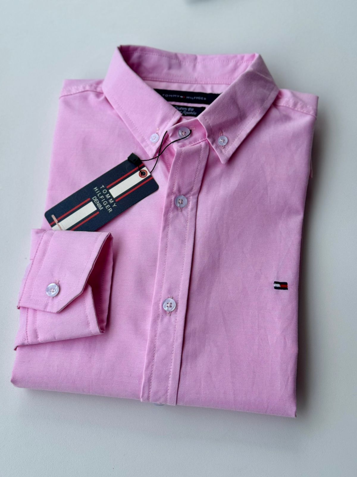 Camisa rosa doblada con botones y etiqueta sobre fondo blanco