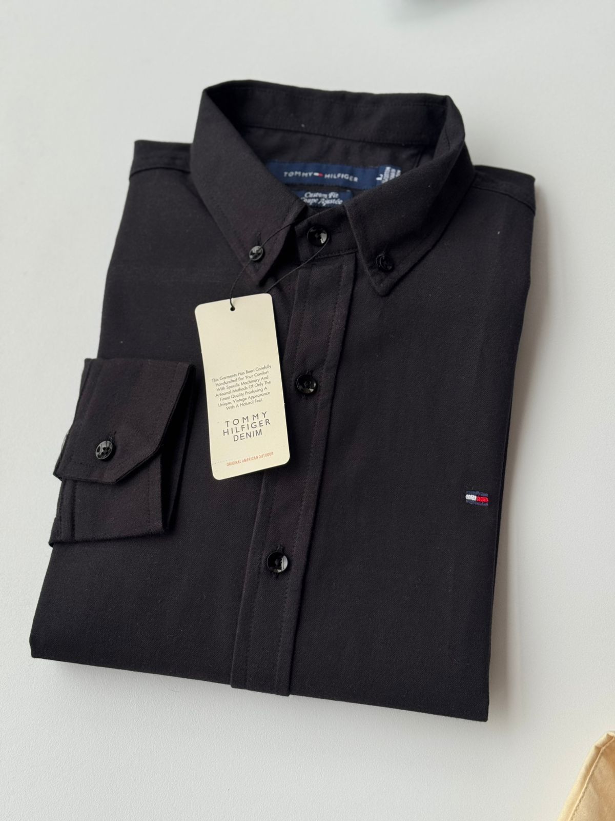 Camisa negra doblada con botones y etiqueta sobre fondo claro