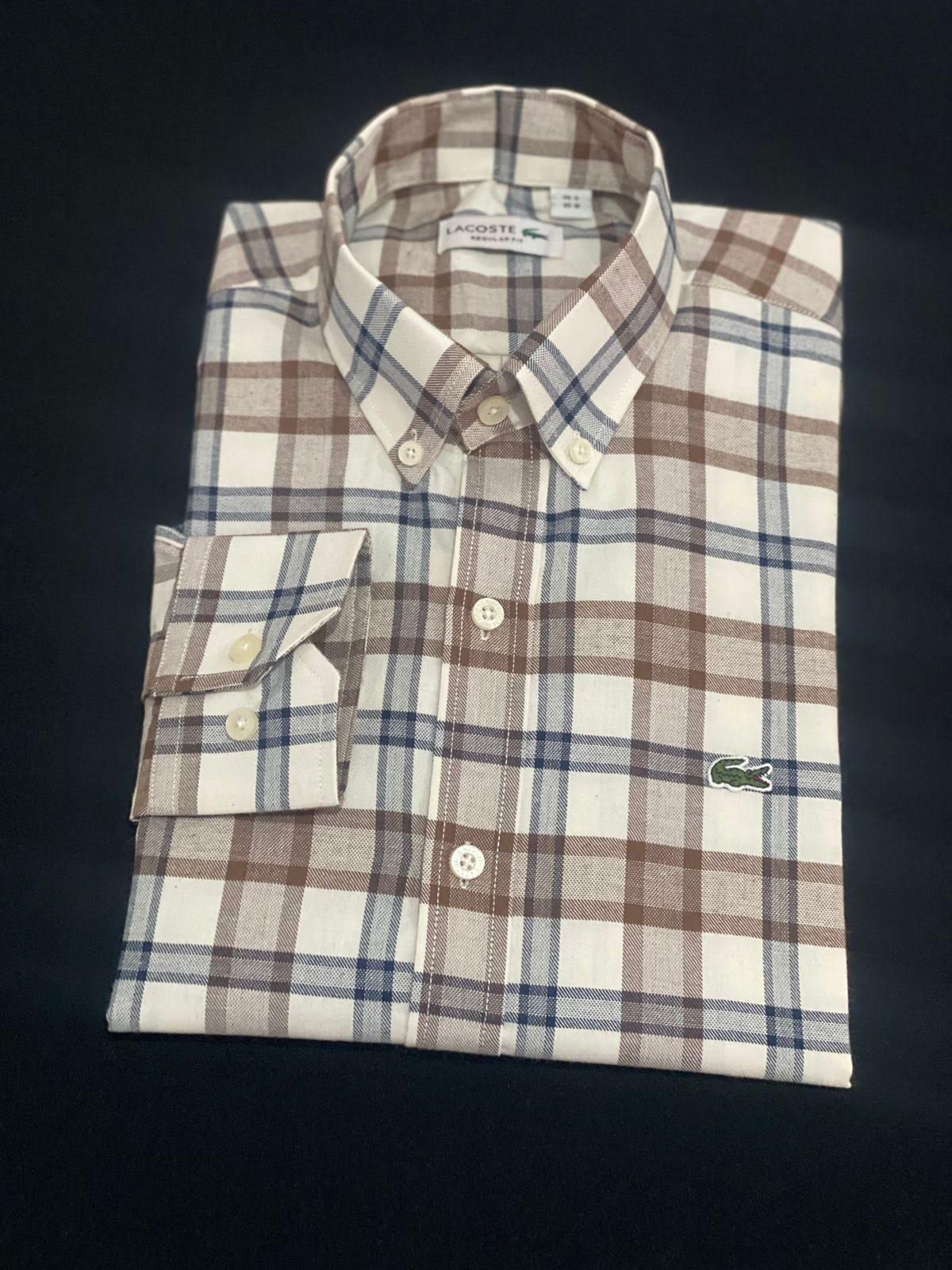 Camisa a cuadros doblada con botones en color beige, marrón y azul con un bolsillo en el pecho sobre fondo oscuro.