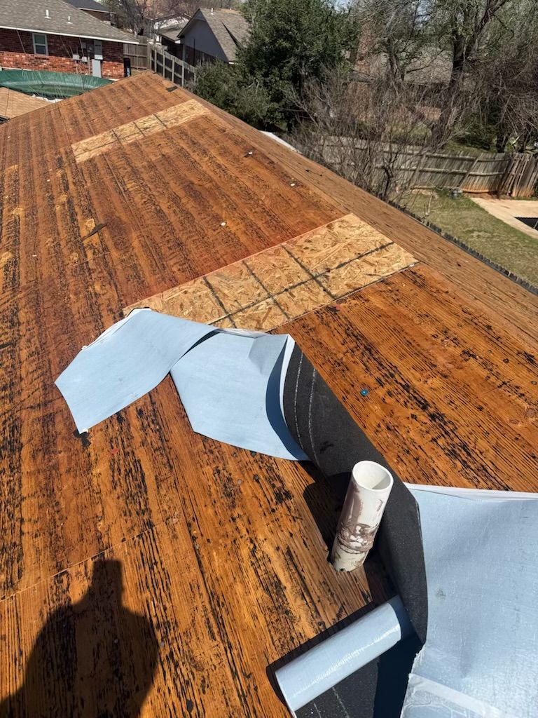 Rusty corrugated metal roof with a blue tarp patch and rooftop vent pipe, viewed from above