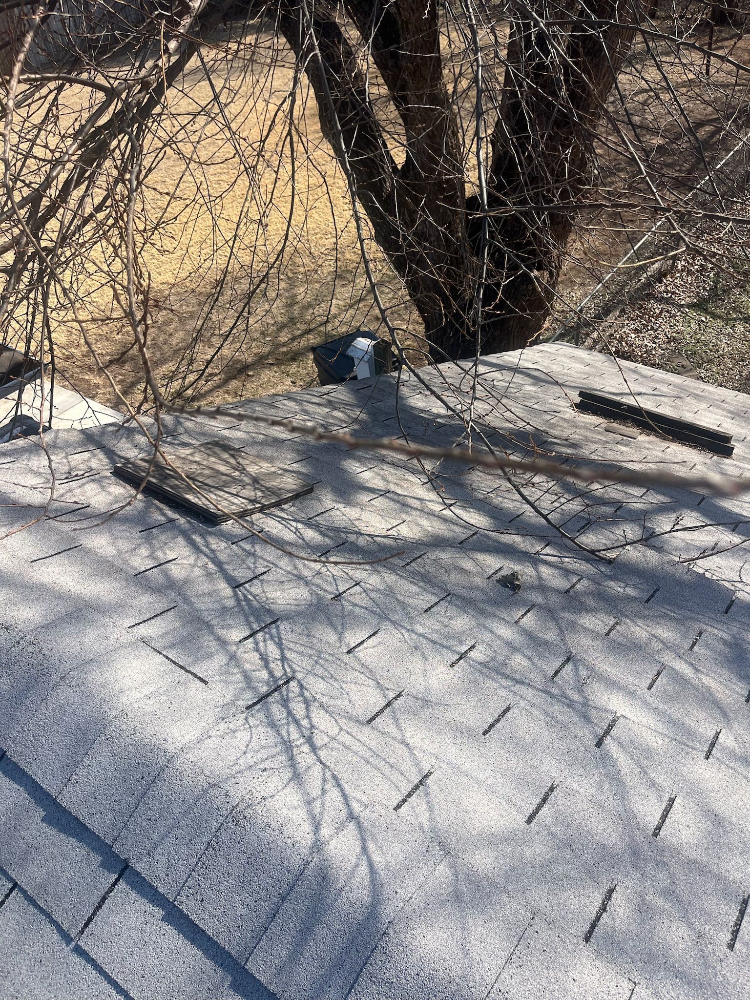 Snow-covered roof with a black chimney pipe beside leafless trees casting shadows