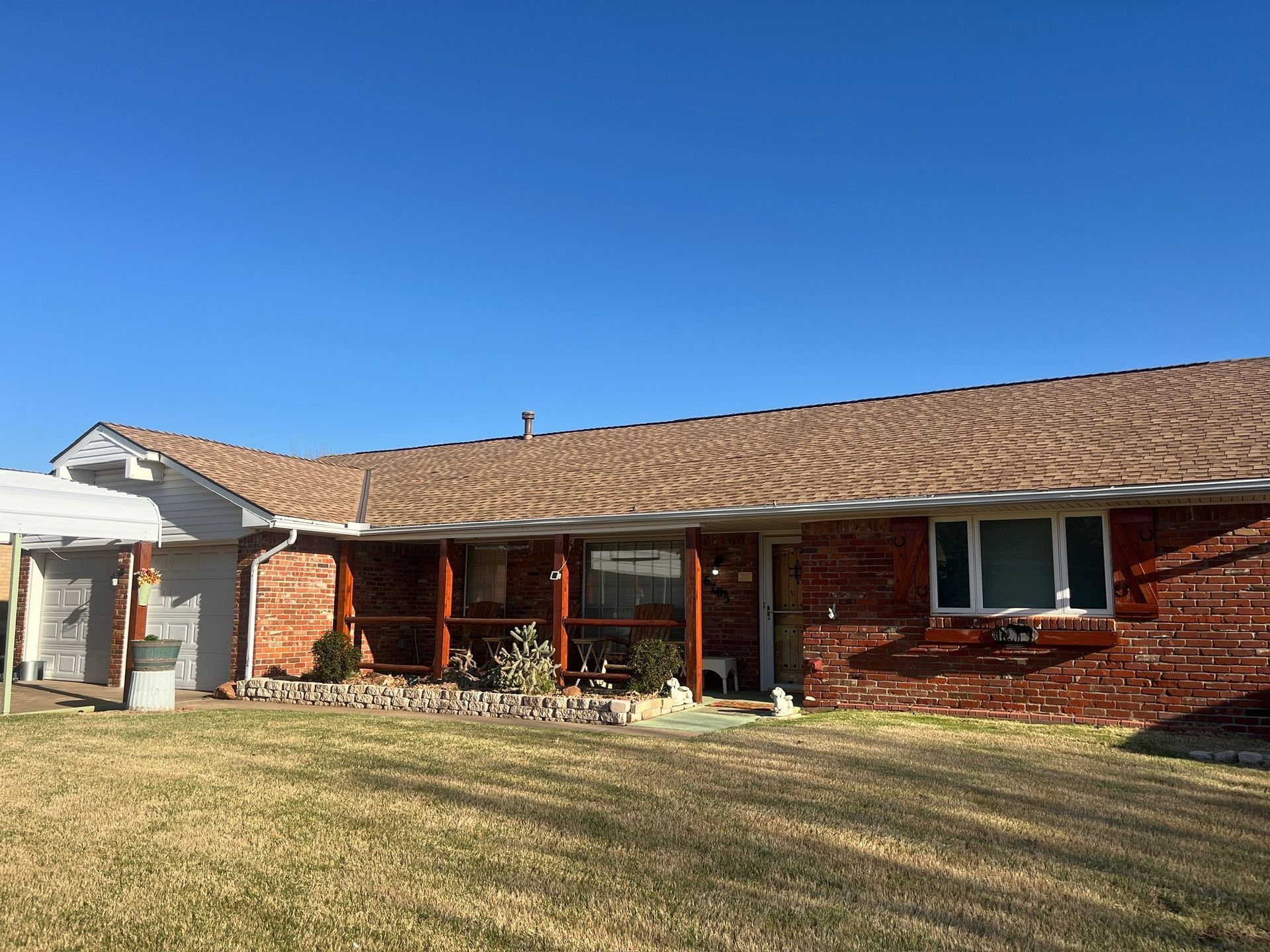 Single-story red brick house with a tan roof and covered front porch under a clear blue sky