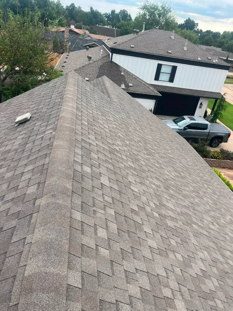 View of a brown shingle roof on a house with a car parked in front of the garage.