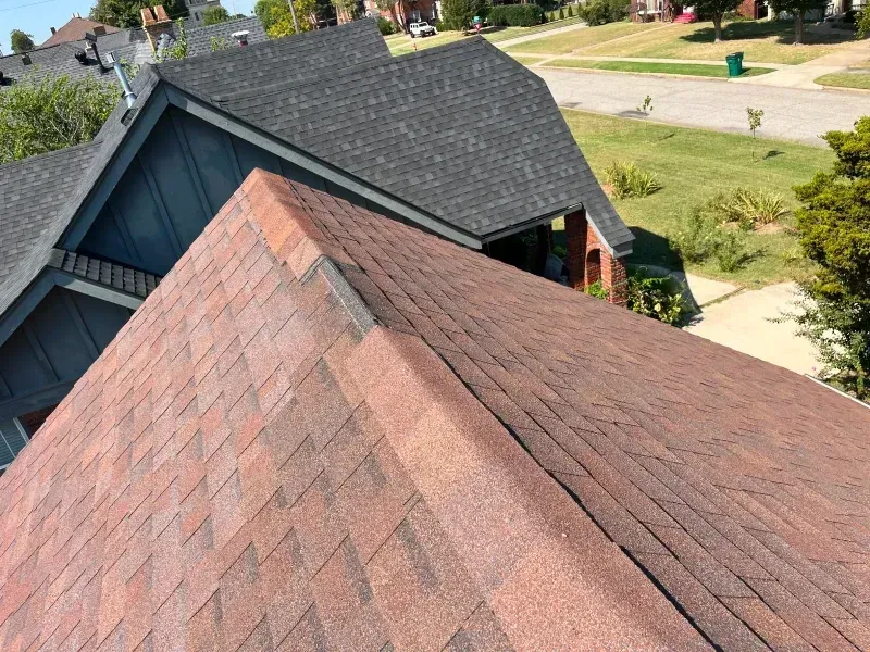 Two houses with shingled roofs, one red-brown, the other dark gray, against a neighborhood backdrop.