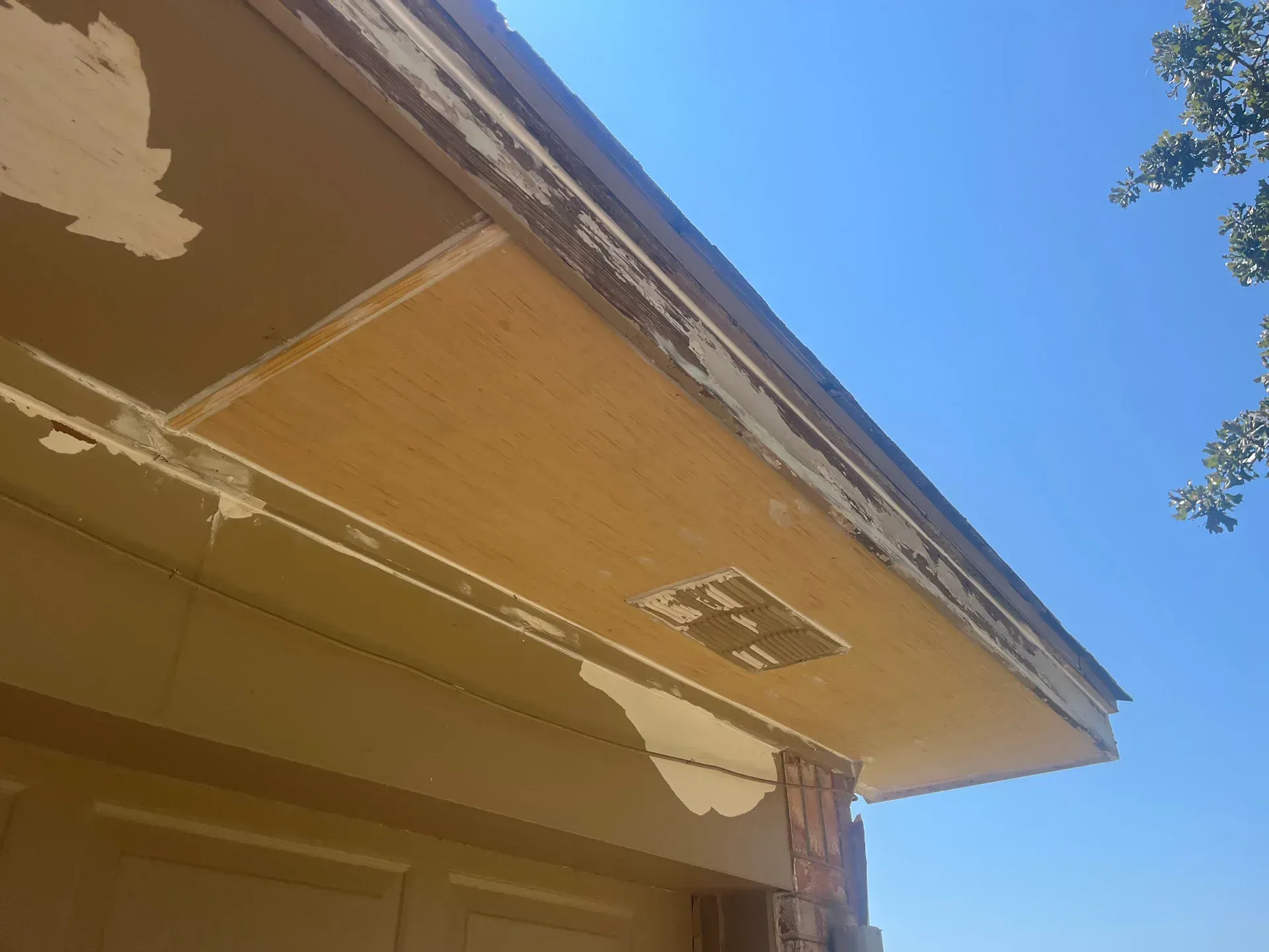 Exterior of house with peeling paint on a light-colored fascia board, against a clear blue sky.