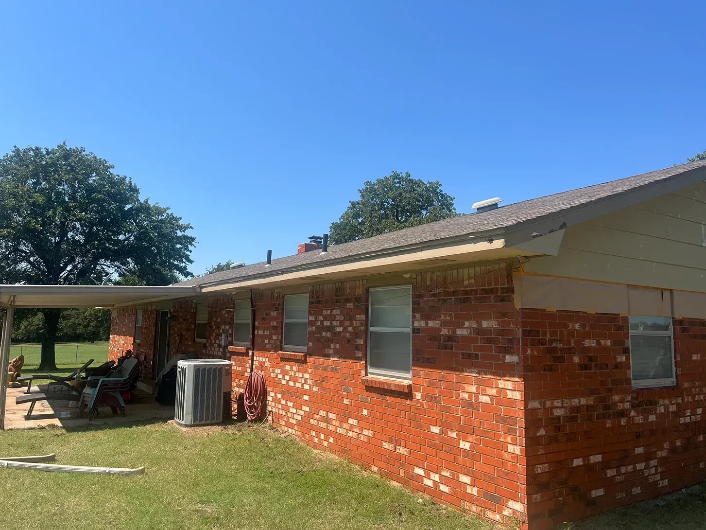 Red brick house with carport, air conditioning unit, and windows on a sunny day.