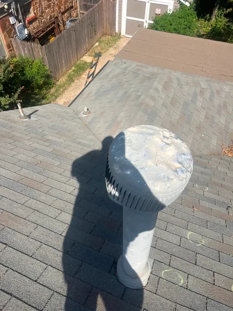 Gray roof with a large, cylindrical vent casting a shadow. Fence and trees visible in background.