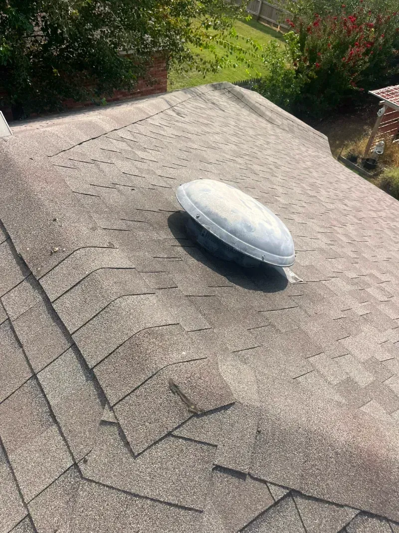 A gray asphalt shingle roof with a white, oval-shaped vent.